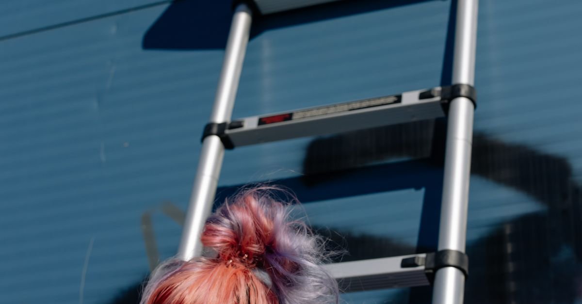 Person on a ladder reaching toward a security camera mounted on an exterior wall
