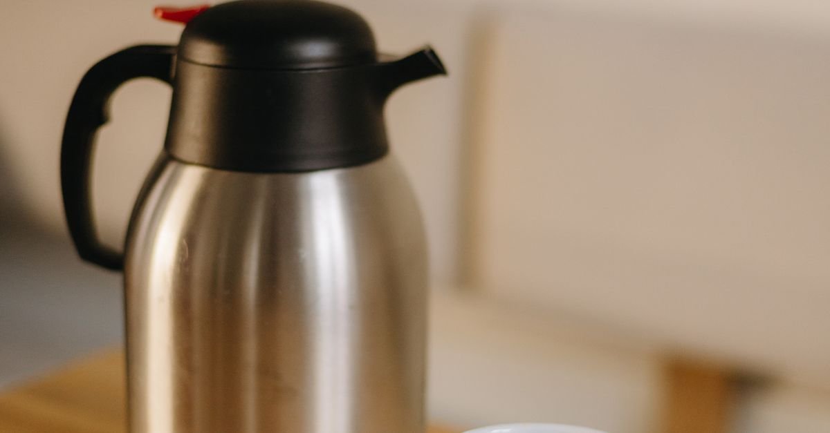 Stainless steel thermos and a mug of black coffee on a wooden table indoors